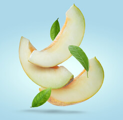 Delicious ripe melon slices and leaves falling on pale light blue background