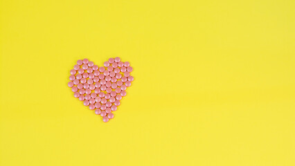 Pills of pink color in the form of a heart on a yellow background. Medicine, treatment, pharmacology, health. Top view Space for text