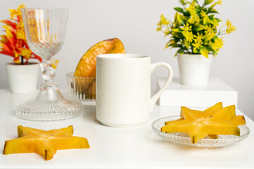 A white blank coffee mug on the top of a rounded mat with the star fruits arranged around it