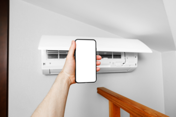 A male technician holds a mobile phone in his hands using a blank white screen mockup. Smart diagnostics of the air conditioner by phone.
