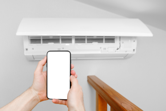 A male technician holds a mobile phone in his hands using a blank white screen mockup. Smart diagnostics of the air conditioner by phone.