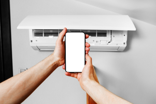 A male technician holds a mobile phone in his hands using a blank white screen mockup. Smart diagnostics of the air conditioner by phone.