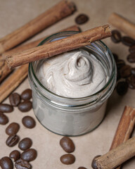 Natural, homemade coffee and cinnamon body butter in transparent jar, coffee beans and cinnamon sticks background.