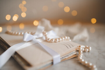Stack of old paper letters with elegant pearl necklace laced with ribbon over lights on marble table indoor. Valentines Day.