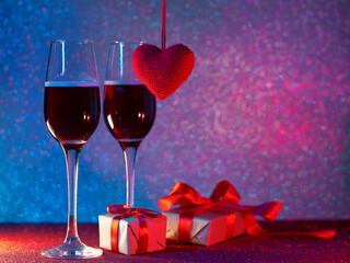 Two glasses of champagne or sparkling wine on the table with gift-wrapped boxes and a red heart. Copy space, shiny bokeh background. Valentine's day or birthday card. Romantic evening