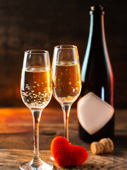 Two glasses of champagne and a red heart on a wooden table, a romantic evening on Valentine's day