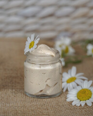                    Cosmetic cream with camomile flower for a eye, face and body on beige and white background.   