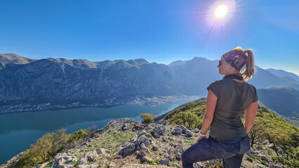 Naklejka premium Woman with scenic view from mountain summit of Vrmac Sveti Ilija on Kotor bay in summer, Adriatic Mediterranean Sea, Montenegro, Balkans, Europe. Fjord winding along coastal towns. Hiking Dinaric Alps