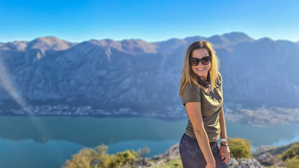 Naklejka premium Woman with scenic view from mountain summit of Vrmac Sveti Ilija on Kotor bay in summer, Adriatic Mediterranean Sea, Montenegro, Balkans, Europe. Fjord winding along coastal towns. Hiking Dinaric Alps