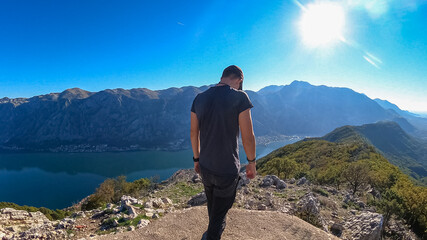 Man with scenic view from mountain summit of Vrmac Sveti Ilija on Kotor bay in summer, Adriatic Mediterranean Sea, Montenegro, Balkans, Europe. Fjord winding along coastal towns. Hiking Dinaric Alps
