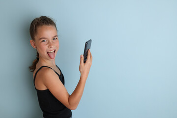 Little emotional teenage girl in pink shirt 11, 12 years old on an isolated blue background with a tablet in her hands.Children's studio portrait. Place the text to copy the place for the inscription