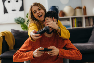 Woman covers mans eyes while playing a video game together