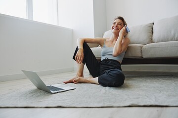 Freelance woman with laptop and phone works from home sitting on the floor in her home clothes with a short haircut, free copy space