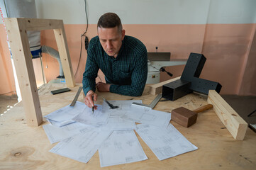 Fototapeta Portrait of a carpenter in a plaid shirt draws a workshop blueprint.  obraz