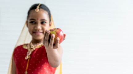 Blurred soft images, 8-year-old Indian girl wearing a red sari, holding and eating fruit is an apple on white background, to Indian girl and fruit concept.