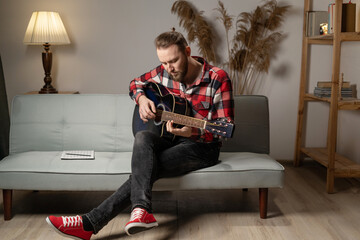 Young man playing guitar at home in the evening.