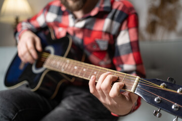 Male musician playing acoustic guitar on sofa at home.