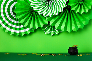 St Patricks Day paper fans decorations and pot of gold coins on green table. St Patrick's Day background.