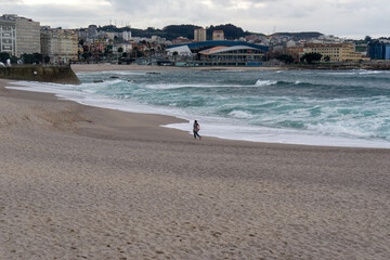 A person walks thoughtfully along the seashore in the late afternoon. Orzán Beach, A Coruña, Spain.