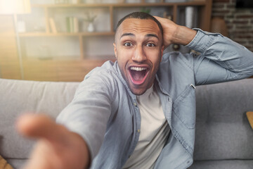 Young handsome man wearing shirt making selfie by the camera sitting  on sofa at living room  very...