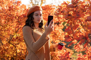 Young woman with autumn leaves in front of foliage making selfie.