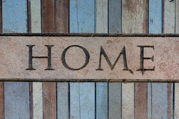 Home word on old dirty weathered carpet on multicolored wooden floor. Close-up top view. Domestic life theme.