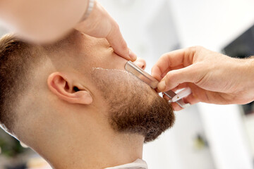 Barber shaving bearded man with retro knife