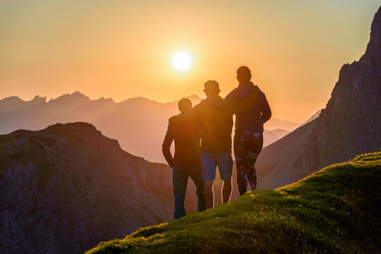 3 Friends Hugging Each Other Looking At Sunset In The Mountains