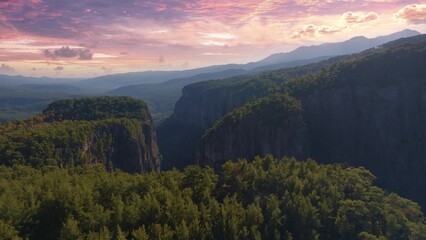 Top view of high rocks in mountainous area. Sunset sky. Pink purple clouds. The tops of the trees. High quality photo