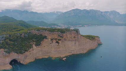 Top view of a rocky shore covered with green trees. Cave in the rock. The boat is near the shore....