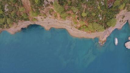 Top view of a rocky shore covered with green trees. Cave in the rock. The boat is near the shore....