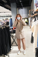   Beautiful woman is wearing protective face mask in shopping center. Girl trying on clothes. Concept of virus protection. Fashion, beauty and shopping concept.