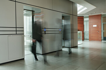 Part of spacious corridor inside modern office center and two blurred businessmen by elevators with...