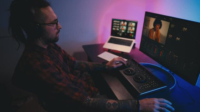 Young man in glasses working on video editing on computer doing montage and color correction. Professional man hand making edits on a special panel. Concept of creating video content.