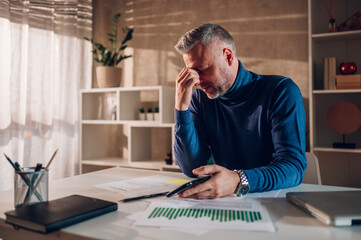 Stressed and tired gray haired middle aged man working in a home office