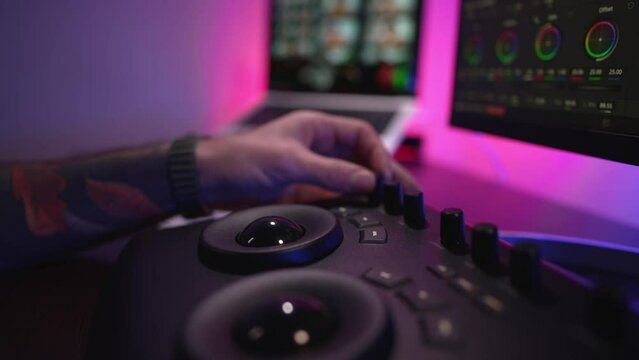 Close-up of a man's hand making edits on a special panel. Young man in glasses working on video editing on computer doing montage and color correction. Concept of creating video content.