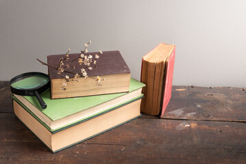 Stack of old books with dried flowers and a magnifying glass on a wooden tabletop. 