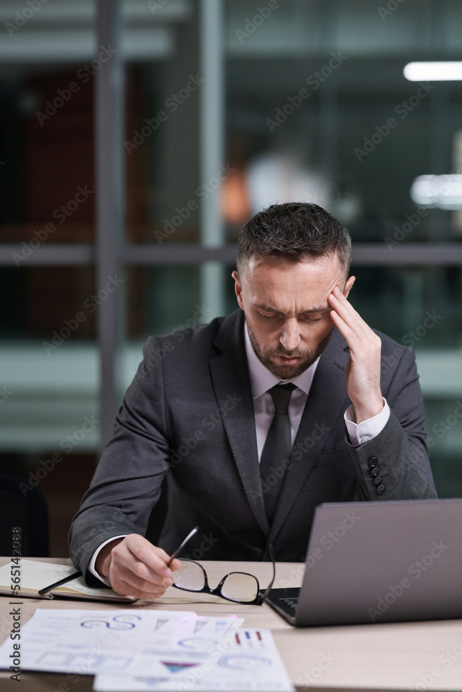 Poster Overworked and tired businessman in formalwear sitting by desk, bending over laptop and touching temple while trying to concentrate