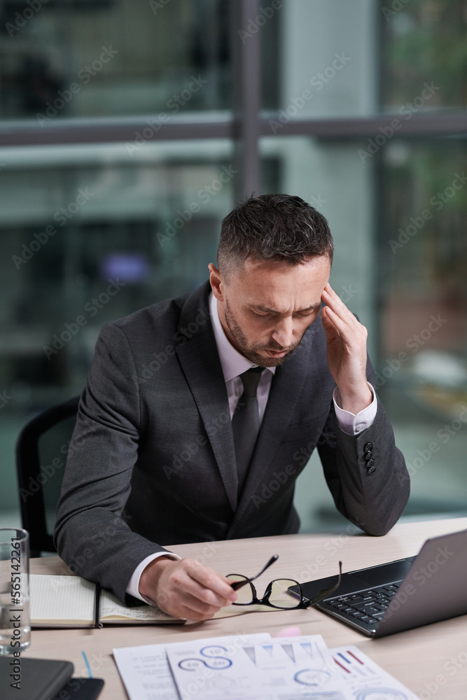 Poster Overworked chief executive office with hand on temple feeling sick while sitting in front of laptop by workplace and analyzing online data