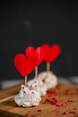 set of 3 meringues with heart stickers and raspberry powder, on wooden board, dark background.