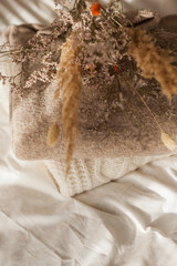 Cozy home decor. Warm winter clothes. Bouquet of dried flowers. Women things. Pastel colors.