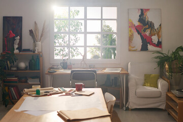 Part of spacious and comfortable sunlit room serving as studio of modern artist skilled in painting with variety of supplies for creating artworks