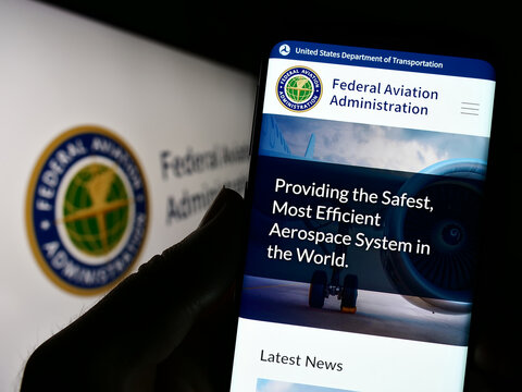 Stuttgart, Germany - 01-24-2023: Person holding smartphone with website of US Federal Aviation Administration (FAA) on screen in front of seal. Focus on center of phone display.