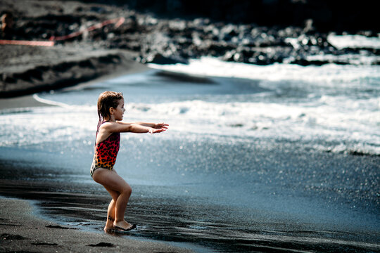 Cute little girl wearing in bright colorful swimsuit. standing and playing on black sand beach on Tenerife near Atlantic ocean. funny summer time, summer vacation destination