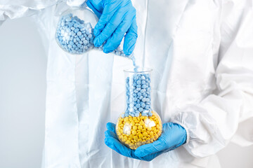 a female doctor in latex blue gloves on a white background pours pills from one flask to another Blue and Yellow pills Close up