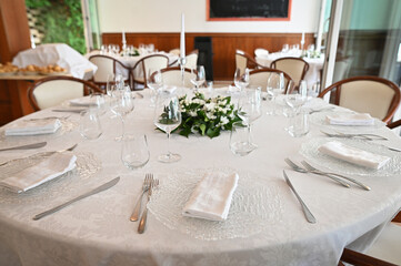 Banquet table is decorated with plates, cutlery, glasses, flower arrangements