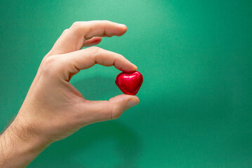 una mano de hombre sujetando un corazón rojo de chocolate sobre fondo verde. Un corazón rojo...