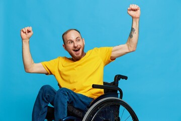 A man in a wheelchair happiness raised his hands up in a t-shirt with tattoos on his hands sits on...