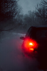 Red glowing tail lights of a car with smoke in winter twilight