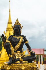 A black and golden buddha statue at a temple with a stuppa in the background
